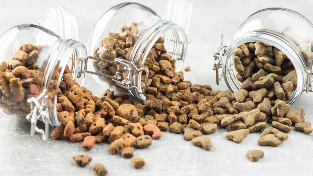 A variety of dry pet food kibble spilling from glass jars